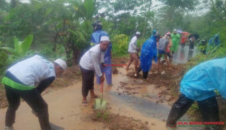 Relawan HILMI-FPI bersama para warga membersihkan material lumpur yang menghalangi jalan dengan mengenakan jas hujan dan peralatan sederhana